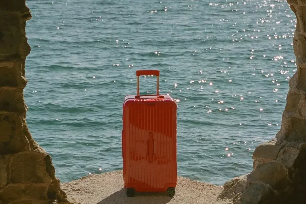 Valise rouge face à la mer, encadrée par une ouverture rocheuse